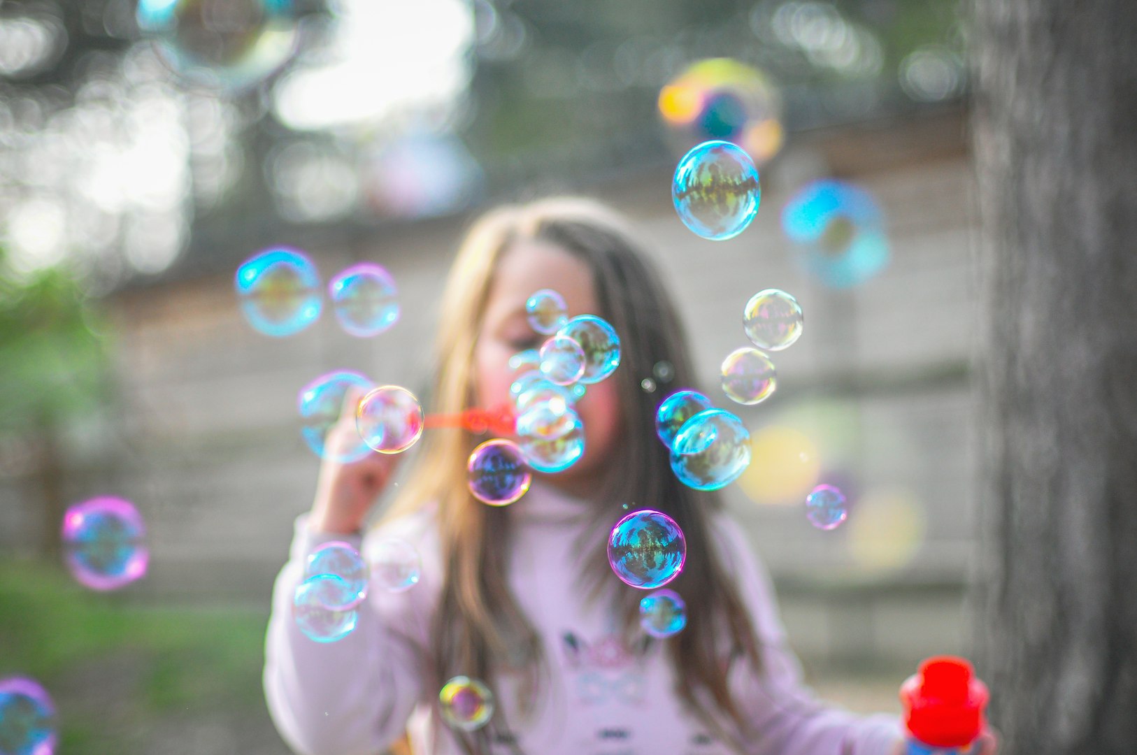 A young child blowing soap bubbles in a garden